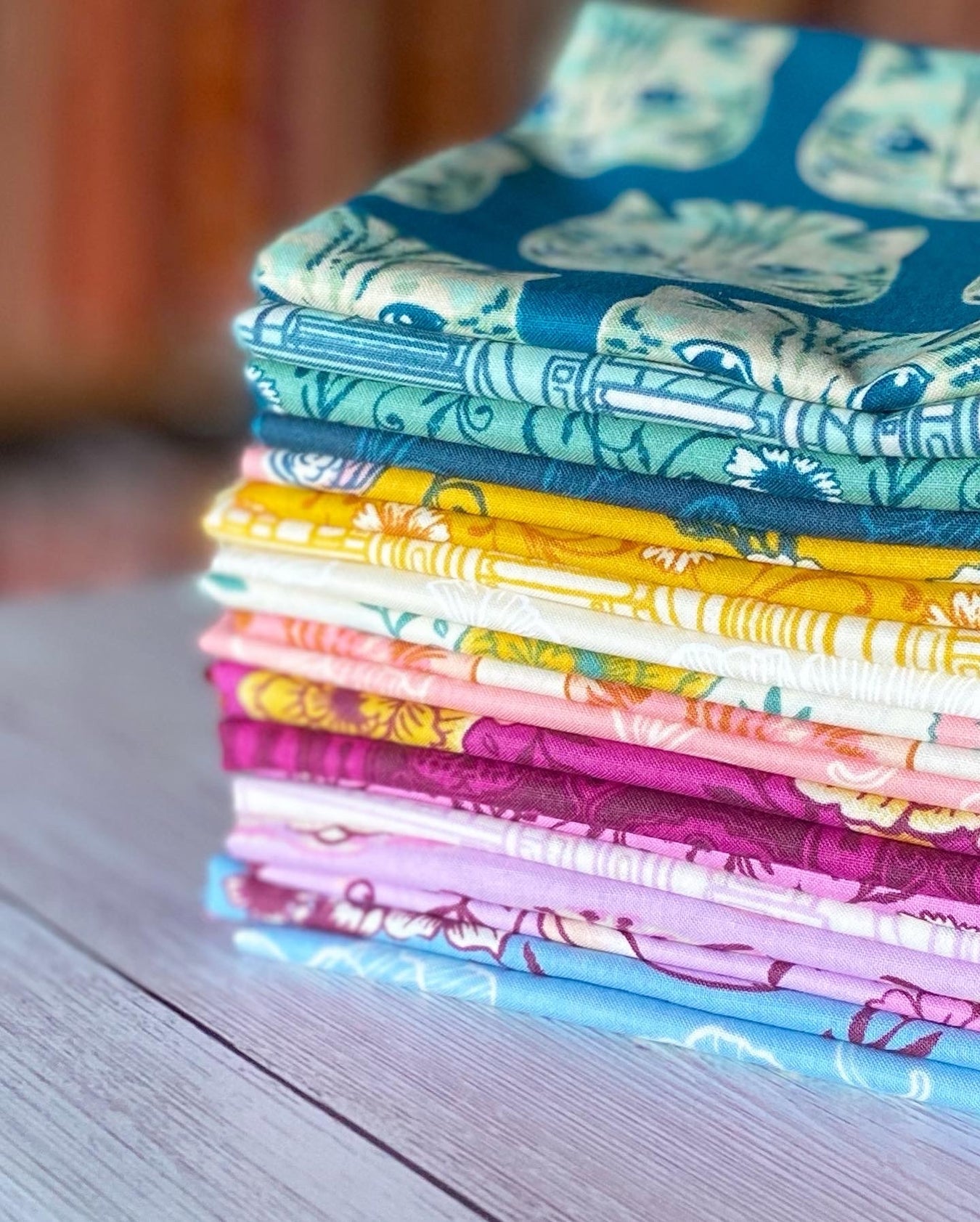 a stack of Sarah Watts reading nook fabrics are folded.  Green cats are at the top