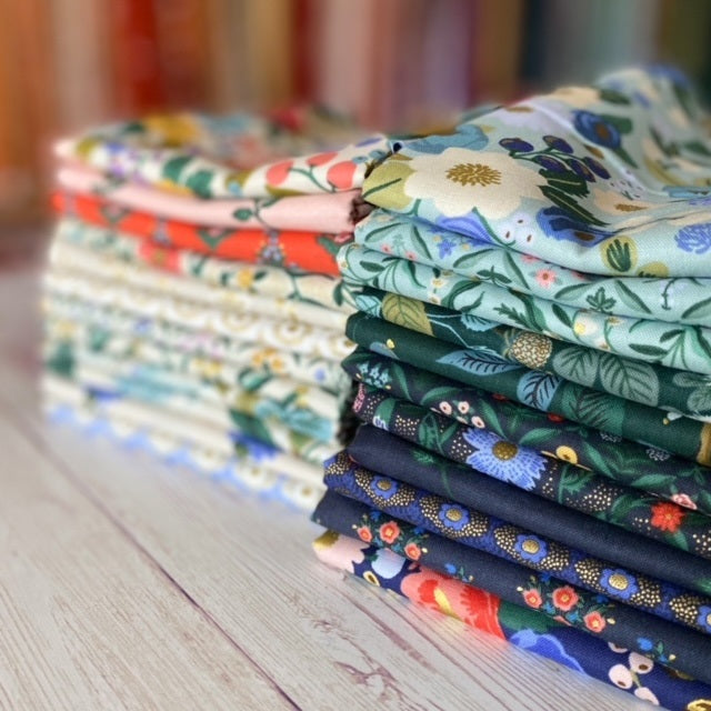 vintage garden fat quarters are folded and stacked in two piles.  The front stack is green and the back stack is cream with pops of red pink and cornflower blue